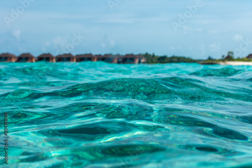Tropical villas on beach shot from water waves of Indian ocean on Maldive isalnds