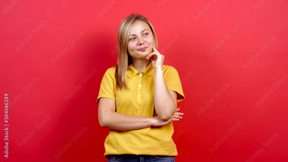 Beautiful Caucasian woman, in yellow T-shirt and with long blond hair, standing on a red background, gestures and keeps her finger on her lips. A little fat teenager. Beautiful Caucasian woman, in yellow T-shirt and with long blond hair, standing on a red background, gestures and keeps her finger on her lips. A little fat teenager.
