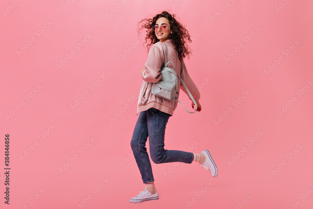 Stylish woman in jeans and jacket moving on pink background