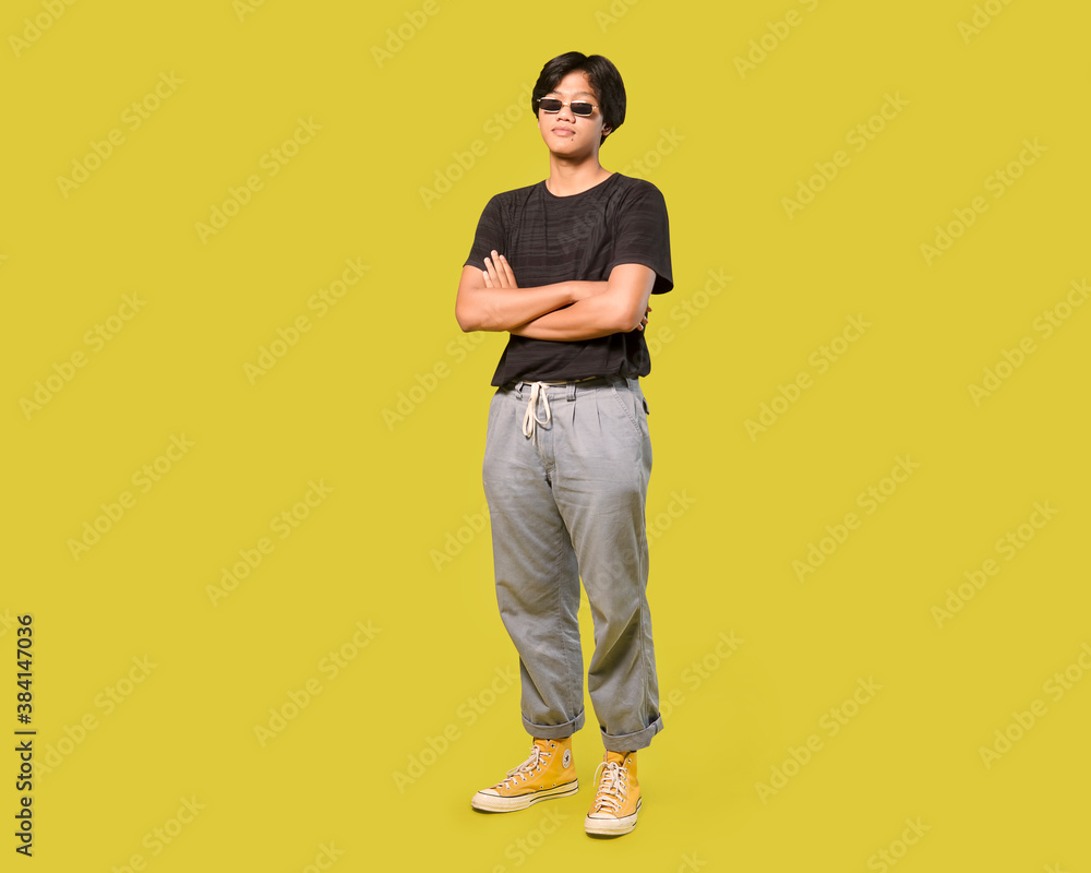 young asian man with black sunglasses standing with arms folded. isolated on yellow background with clipping path young asian man with black sunglasses standing with arms folded. isolated on yellow background with clipping path