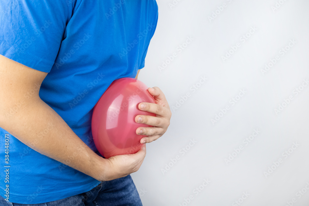 Bloating and flatulence concept. The man holds a red balloon near the abdomen, which symbolizes gas problems. Intestinal tract and digestive system Bloating and flatulence concept. The man holds a red balloon near the abdomen, which symbolizes gas problems. Intestinal tract and digestive system