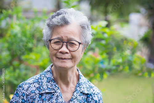 Portrait of a senior Asian woman wearing glasses, smiling and looking at camera while standing in a garden. Space for text. Concept of old people and healthcare