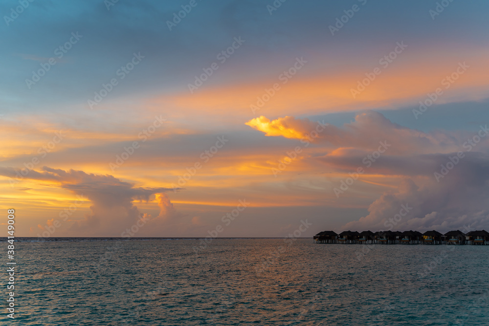 Scenic view on small villas on horizon under colorful clouds in sky during sunset in Indian ocean on maldive islands