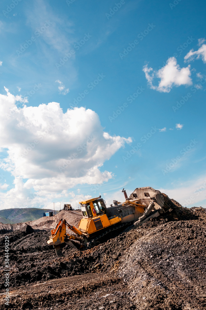Fototapeta premium Open pit mining (natural gold) in mountainous areas. A bulldozer collects a pile of mountain soil. Then, wheel loaders transport this mountain soil and dump it into industrial washing equipment in ord