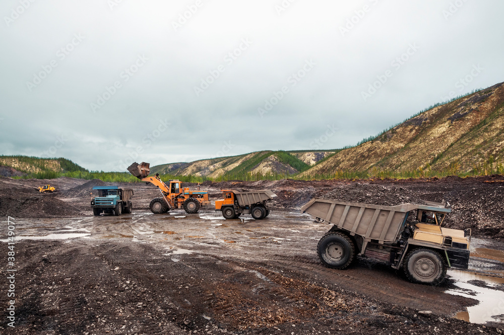 Obraz premium Loading of mountain soil into the body of a mining dump truck using a wheel loader, and further transportation of the cargo. Extraction of minerals in the mountainous region of Eastern Siberia