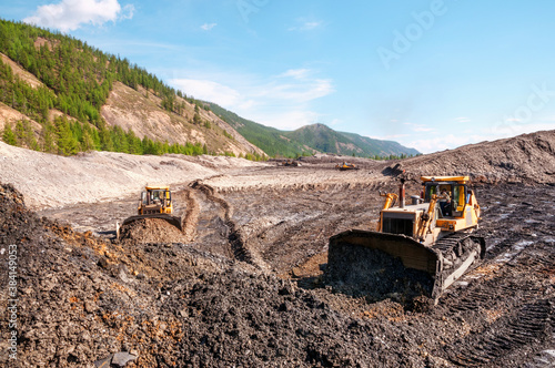 Open pit mining (natural gold) in mountainous areas. A bulldozer collects a pile of mountain soil. Then, wheel loaders transport this mountain soil and dump it into industrial washing equipment in ord