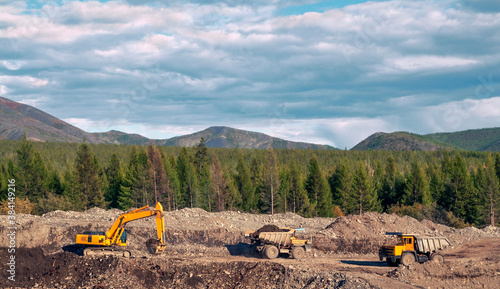 Excavator loads mountain soil into the body of a mining dump truck and then transports the load. Extraction of minerals in the mountainous region of Eastern Siberia