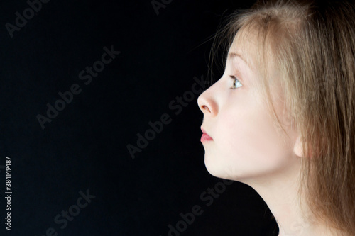 Teenager girl with bright emotions on her face on a black background. Selective focus. Side view