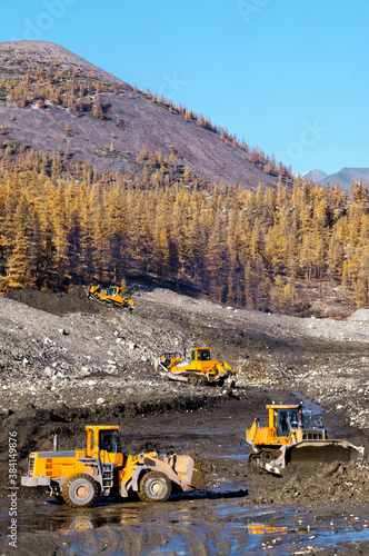 Open pit mining (natural gold) in mountainous areas. A bulldozer collects a pile of mountain soil. Then, wheel loaders transport this mountain soil and dump it into industrial washing equipment in ord