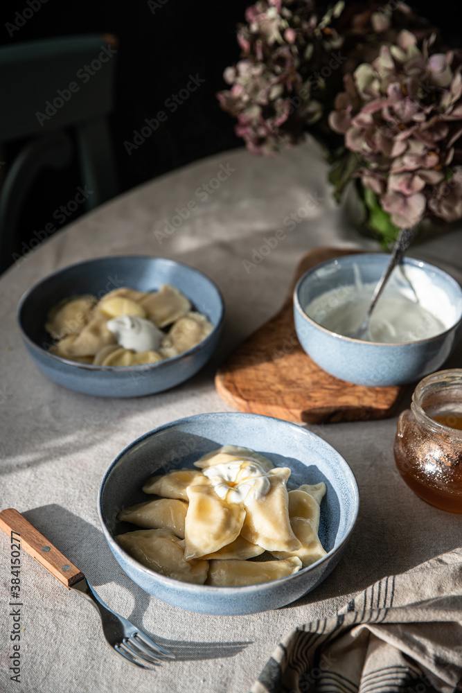 Pyrogy (pierogi) and sour cream in blue plates on round table with linen tablecloth , Pyrogy (pierogi) and sour cream in blue plates on round table with linen tablecloth ,