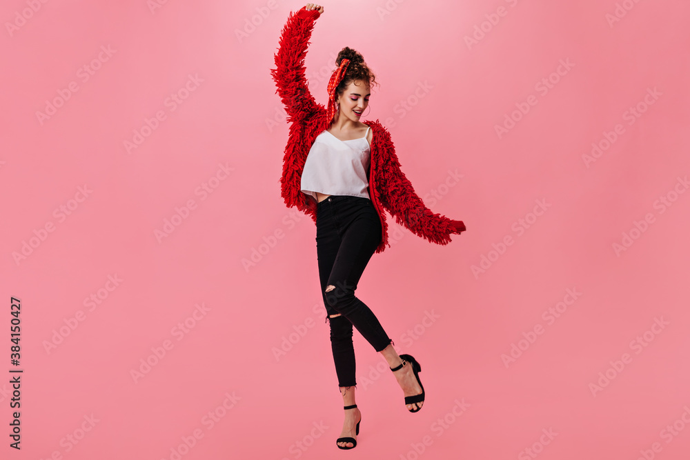 Pretty woman in warm jacket and jeans dancing on pink background Pretty woman in warm jacket and jeans dancing on pink background