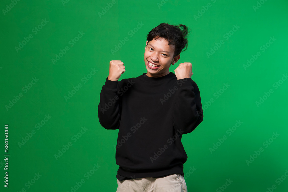 Young asian man on isolated green background. very happy and excited doing winner gesture with arms raised, smiling and screaming for success. Celebration concept. Young asian man on isolated green background. very happy and excited doing winner gesture with arms raised, smiling and screaming for success. Celebration concept.
