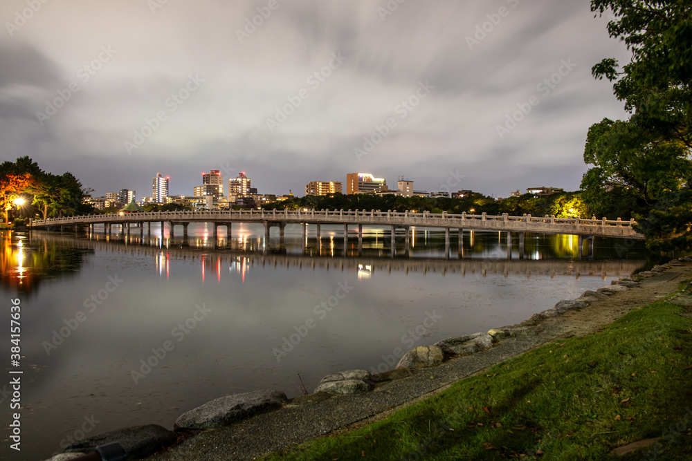 Fototapeta premium Ohori Park, a city park in central Fukuoka with a large pond at its center, in cloudy day in dark mood. The present park was modeled on the West Lake of China and opened in 1929