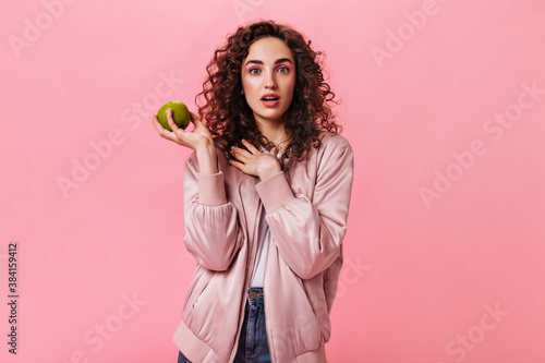Woman in silk jacket holding green apple on pink background