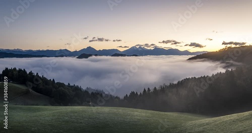 Time lapse low inversion clouds rolling in Alpine valley. Amazing sunrise golden hour and landscape with Alps mountains in Slovenia. Wide angle, static shot