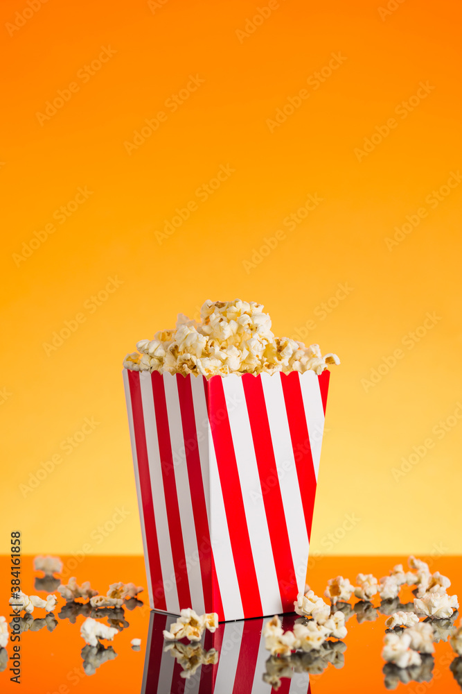 Red and white Popcorn box filled with popcorn on orange background