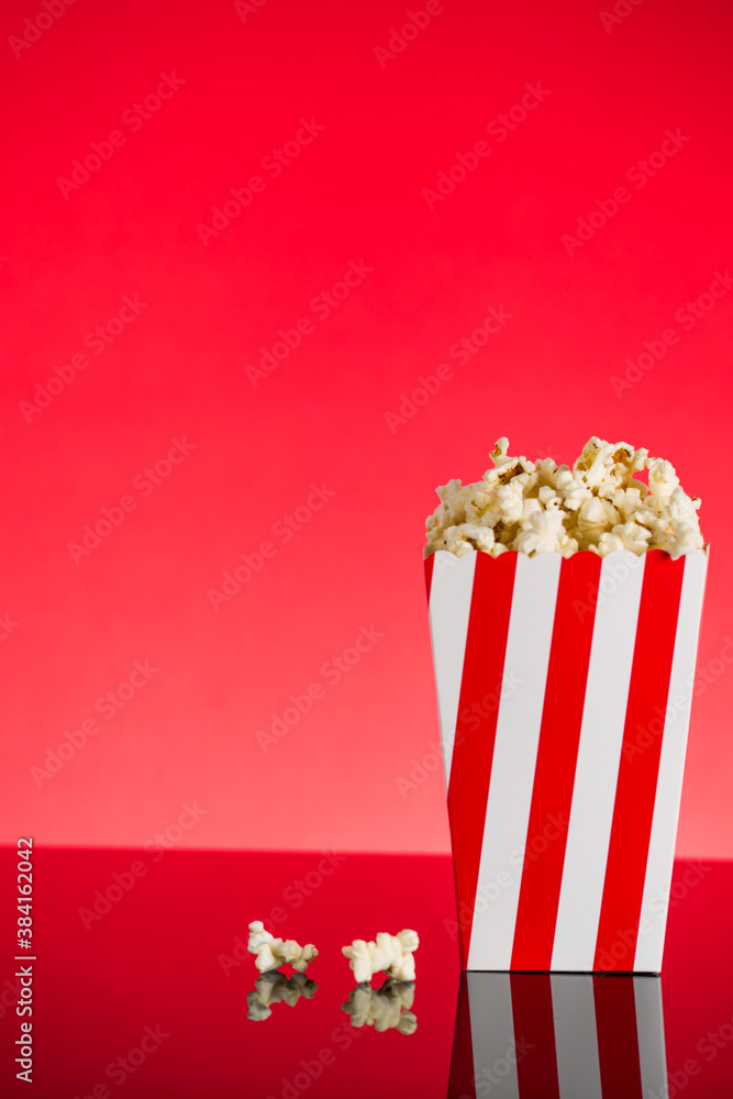 Red and white Popcorn box filled with popcorn on red background