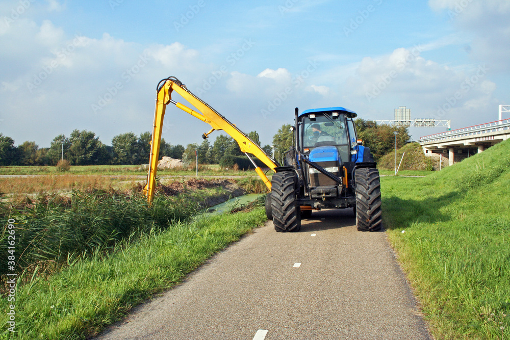 Summer ditch cleaning by a tractor in  a Dutch polder ;andscape - obrazy, fototapety, plakaty 