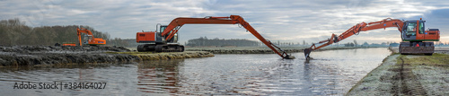 Fotografie, Obraz Dredging of an inland canal by cranes in winter at sunset.