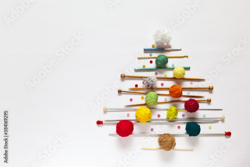 Merry Christmas and Happy New Year  funny Christmas tree made of knitting accessories  woolen balls  knitting needles and crochet hooks on a white background. Copy space  flat lay  mock up  top view