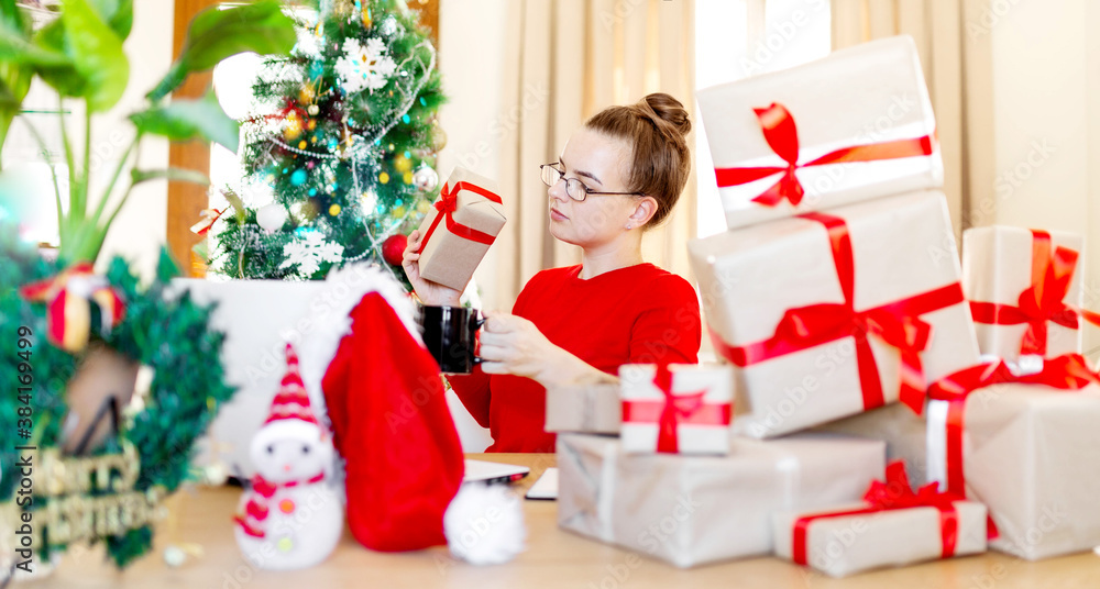 Woman in red sweater, in santa office preparing for Christmas, many presents and christmas tree in background, laptop on table, working New Year desk at home Woman in red sweater, in santa office preparing for Christmas, many presents and christmas tree in background, laptop on table, working New Year desk at home