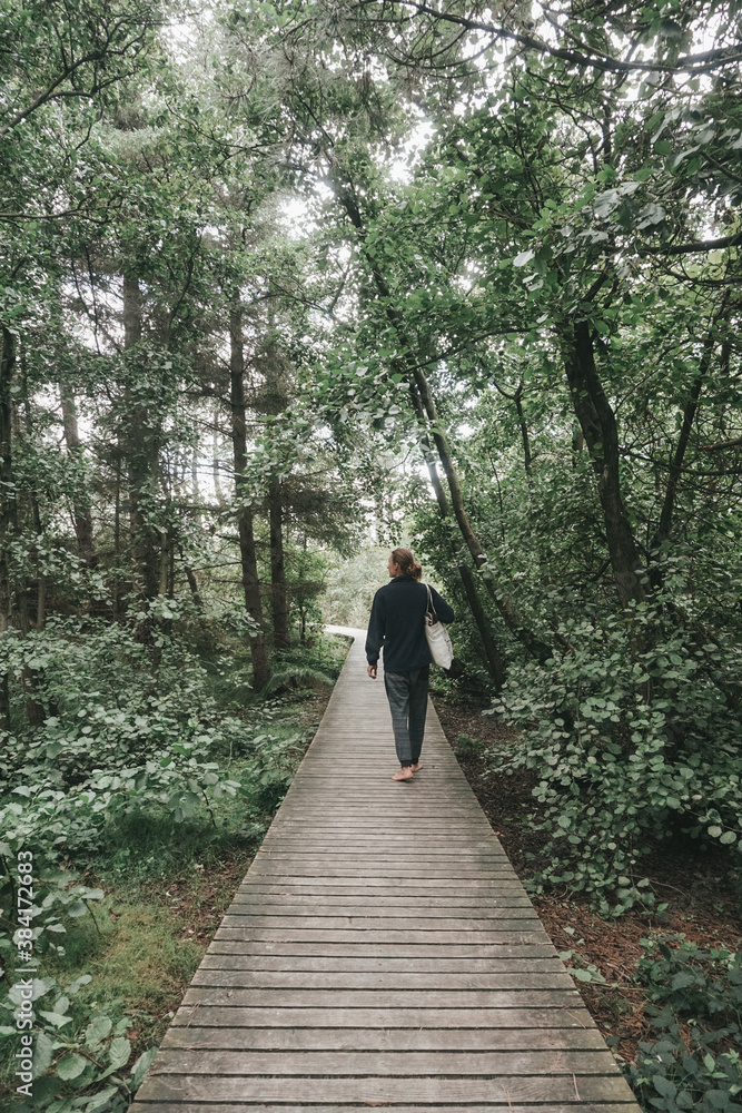 Obraz premium Junger Mann läuft barfuß über einen Holzsteg im Wald auf Amrum