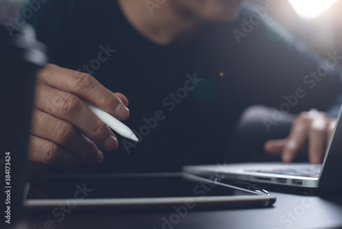 Man hand with stylus pen working on digital tablet and surfing internet on laptop computer online working from home