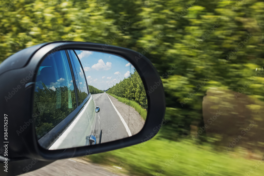 Rear view mirror of the car on outback road with blurred green trees