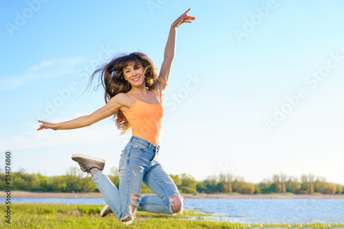 a girl in jeans jumps on the background of the lake and the blue sky