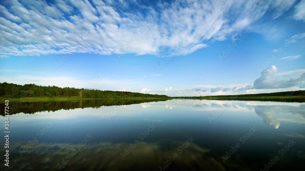 River landscape. Green banks and white clouds are reflected in the mirror of the water.
