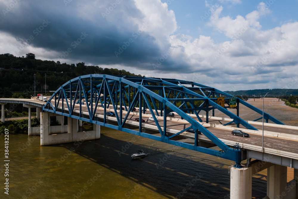 This is an aerial of a blue, eight-lane highway arch bridge that carries Interstate 64 over the Kanawha River in Charleston, West Virginia.
