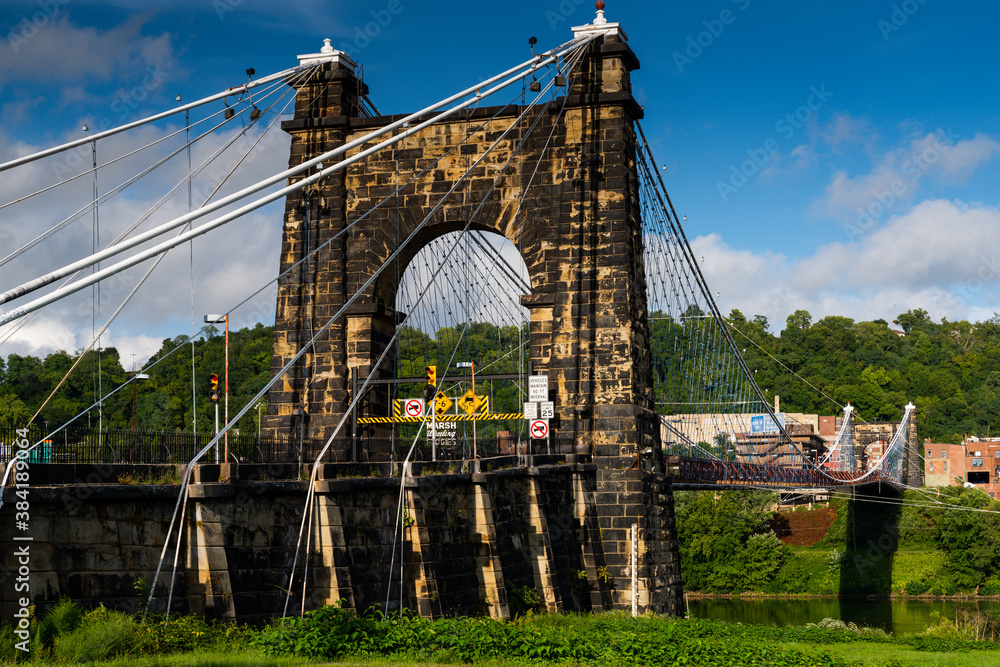 Obraz premium This is a side profile showing the masonry tower of the historic Wheeling Suspension Bridge that carries the National Road over the Ohio River in Wheeling, West Virginia.