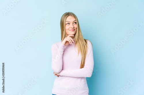 Young blonde woman isolated on blue background looking sideways with doubtful and skeptical expression.