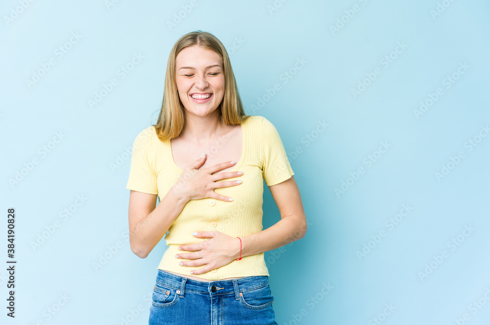 Young blonde woman isolated on blue background laughs happily and has fun keeping hands on stomach.