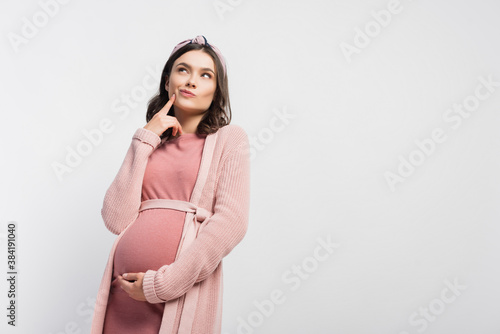 pensive pregnant woman in headband touching face and looking up isolated on white photo