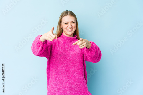 Young blonde woman isolated on blue background cheerful smiles pointing to front.