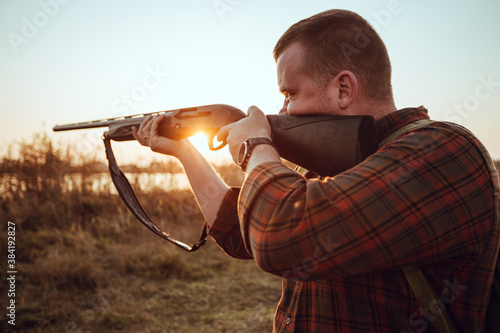 Young irish looking man with a reed, backpack and ammunition belt,  hunting at the countryside near the track in the picturesque sunset rays - photo with selective focus