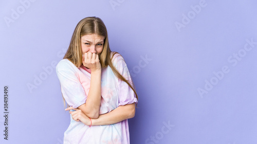 Young blonde woman isolated on purple background biting fingernails, nervous and very anxious.