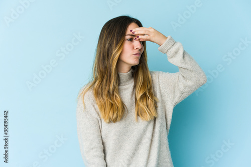 Young caucasian woman isolated on blue background having a head ache, touching front of the face.