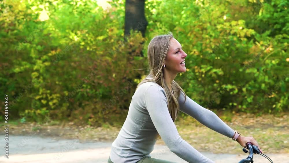 Young woman biking in park, her husband and son following her on background. Side view of cheerful female enjoying cycle ride with family. Concept of sport Young woman biking in park, her husband and son following her on background. Side view of cheerful female enjoying cycle ride with family. Concept of sport