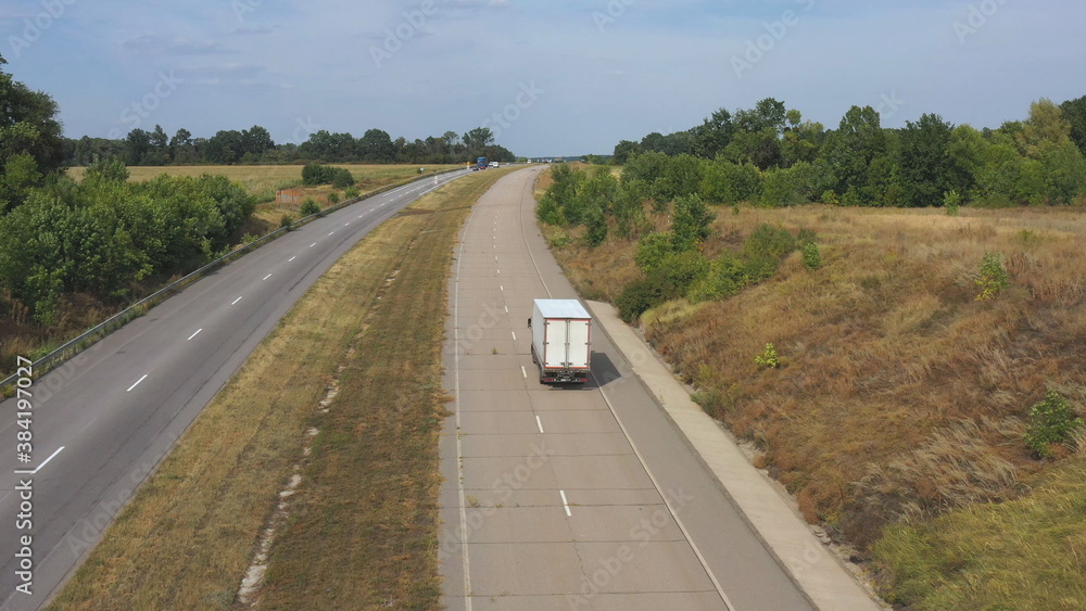 Aerial shot of truck with cargo trailer driving on motorway and transporting goods. Camera following to delivery lorry moving through country highway at sunny day. Flying over road traffic in rural Aerial shot of truck with cargo trailer driving on motorway and transporting goods. Camera following to delivery lorry moving through country highway at sunny day. Flying over road traffic in rural