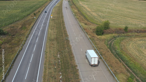 Aerial view of truck with cargo trailer driving on straight road and transporting goods. Camera following to delivery lorry moving across country highway. Flying over traffic in rural