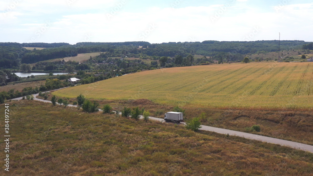 Aerial shot of truck with cargo trailer driving on empty road and transporting goods. Flying over delivery lorry moving along highway passing in beautiful countryside scene. Scenic landscape. Top view