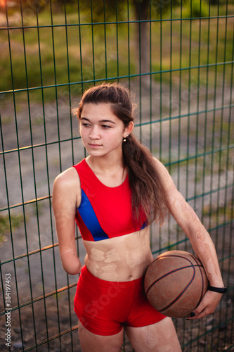 Young woman athlete with an amputated arm and burns on her body. She hold in the hands basketball ball after training outdoor at sunset. © artem_goncharov