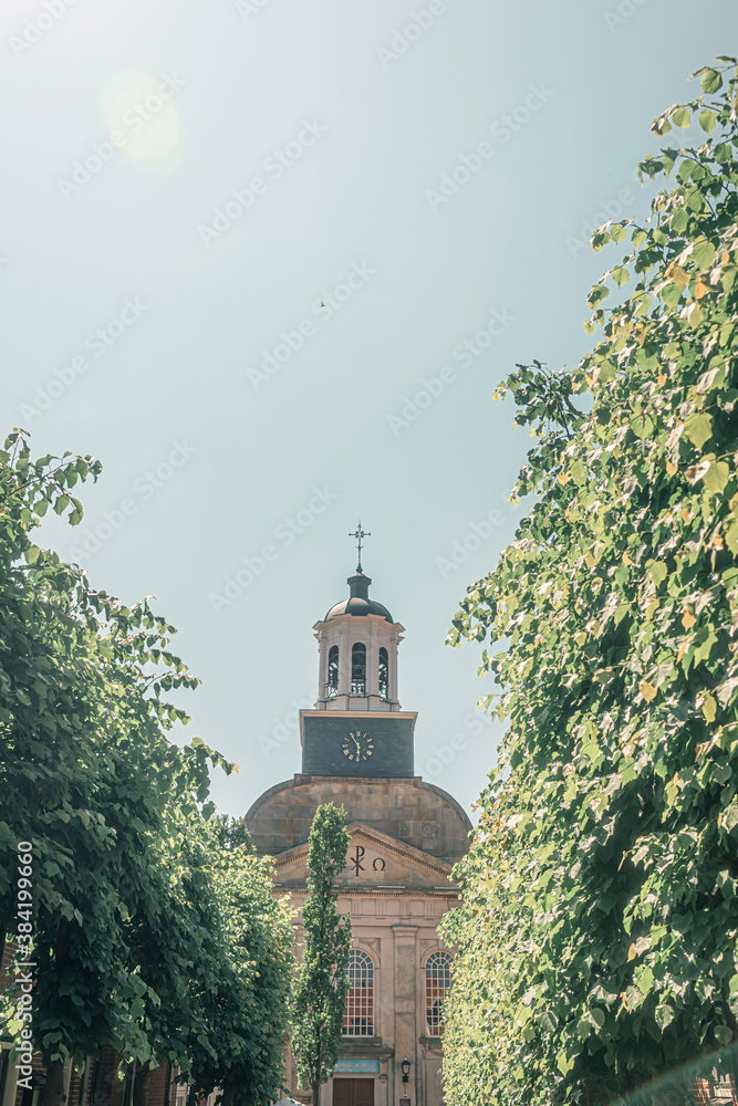 Fototapeta premium Bell tower of church between trees against blue sky.