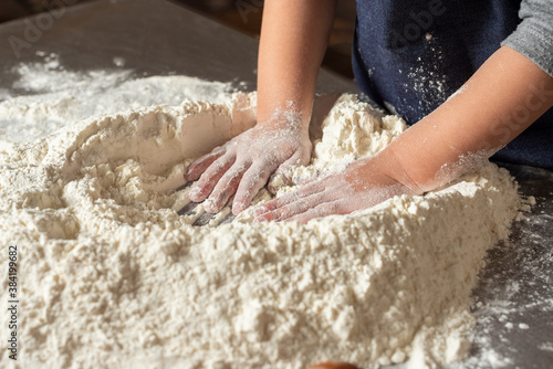  hands of a girl kneading flour with eggs and rolling pin on steel countertop