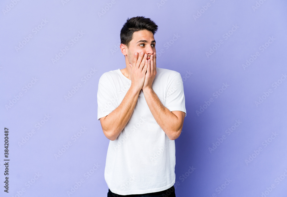 Young caucasian man isolated on purple background thoughtful looking to a copy space covering mouth with hand. Young caucasian man isolated on purple background thoughtful looking to a copy space covering mouth with hand.