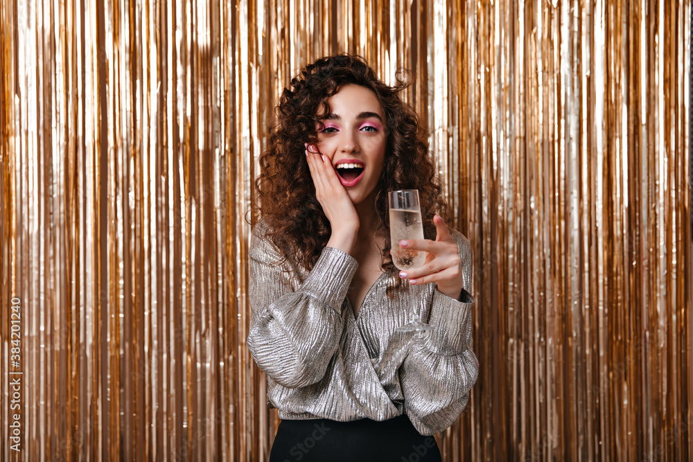 Obraz premium Surprised woman in silver blouse holding champagne glass