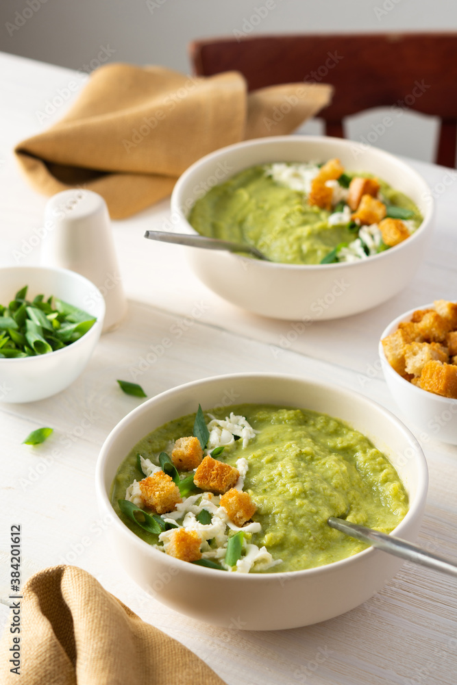 Healthy delicious broccoli and cucumber cream puree soup with mozzarella, green onions and croutons, bowl of soup on a white table Healthy delicious broccoli and cucumber cream puree soup with mozzarella, green onions and croutons, bowl of soup on a white table