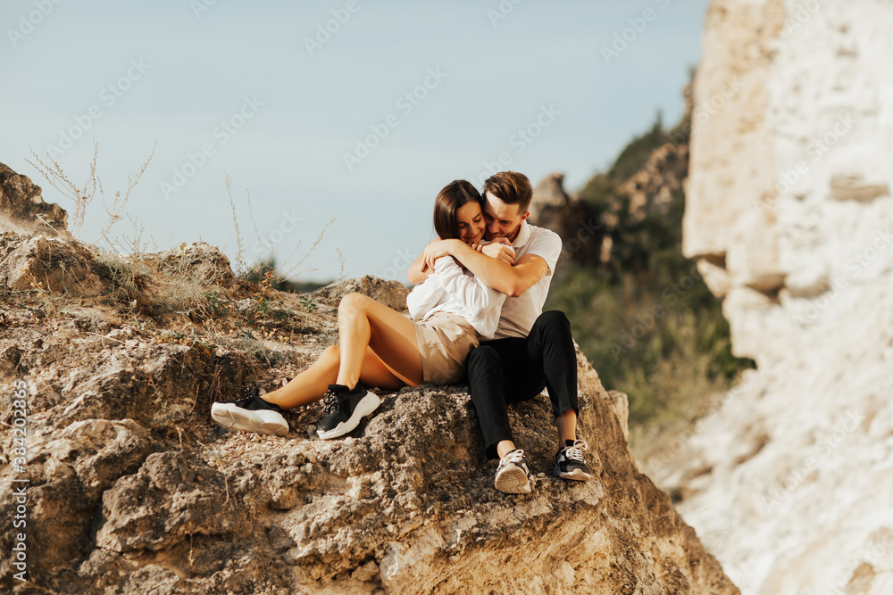 Young couple are hugging and sitting on the stone on the mountain. Romantic tender couple are enjoying time together.